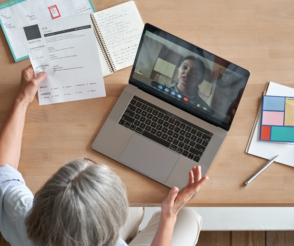 View from above of a video job applications - woman speaking to another woman on a laptop screen, she has a CV in her hand